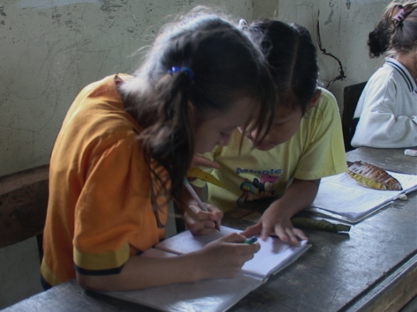 Zwei kleine Mädchen beugen sich über ein Schreibheft, beide mit einem Stift in der Hand